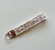 a key chain with flowers on it sitting on top of a white table next to a pair of scissors