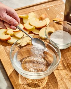 a person is spooning sugar into a bowl of apple slices on a cutting board