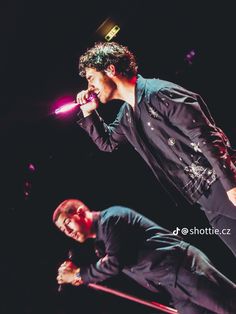 two men are performing on stage with microphones in their hands and one is holding his head