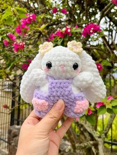 a hand holding a small white and purple stuffed animal