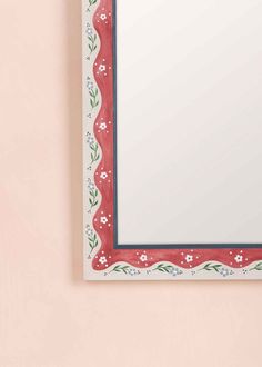 a red and white mirror mounted to the side of a pink wall with flowers on it