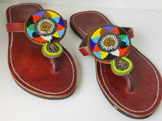 Elevate your summer style with our stunning Maasai Beaded Leather Sandals, expertly handcrafted in Kenya. Each pair features vibrant, intricate beadwork inspired by traditional Maasai designs, making every sandal a unique piece of art.  Made from high-quality leather, these sandals offer durability and comfort for all-day wear. Perfect for both casual outings and special occasions, they not only showcase beautiful craftsmanship but also support local artisans. Step into a world of color and cult Traditional Handmade Brown Flip Flops, Traditional Adjustable Brown Flip Flops, Traditional Beaded Flip Flops For Festivals, Traditional Beaded Brown Flip Flops, Traditional Brown Beaded Flip Flops, Traditional Multicolor Beaded Flip Flops, Traditional Brown Beaded Sandals, Traditional Beaded Flip Flops With Round Toe, Traditional Beaded Sandals With Round Toe