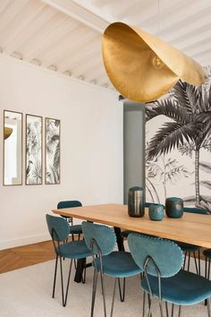 a dining room table with blue chairs and a large golden light hanging from the ceiling