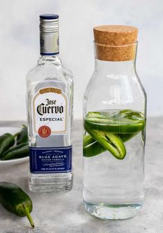 a bottle filled with green peppers next to a small glass jar full of liquid and some leaves