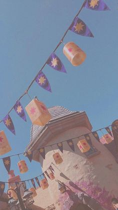 some paper lanterns hanging from a line on a blue and white building with purple flags