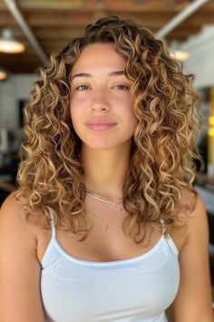 Woman with curly hair smiling slightly, wearing a white tank top in a well-lit room. Caramel Blonde Hair Honey, Toffee Brown Hair Color, Toffee Brown Hair, Warm Honey Brown Hair, Soft Autumn Hair