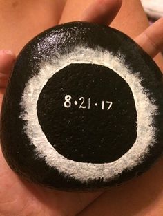 a person holding a black and white rock with the word 8 21 17 written on it