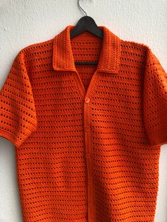 an orange knitted sweater hanging on a white wall next to a wooden hanger