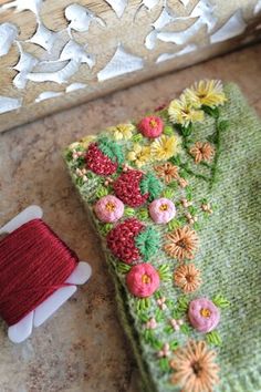 a knitted green bag next to a red spool of thread on a table