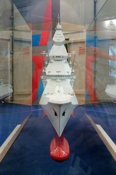 a model ship in a display case with blue flooring and red pedestals on either side