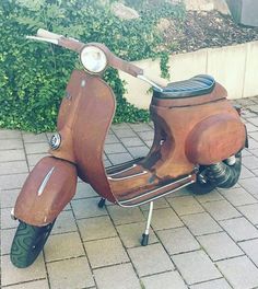 an old scooter is parked on the sidewalk near some bushes and shrubbery