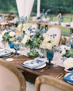 the table is set with blue and white flowers in vases, napkins, and place settings