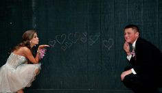 a man kneeling down next to a woman in front of a chalkboard with hearts drawn on it