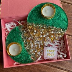 a pink box filled with two green plates covered in gold and white beads next to candles