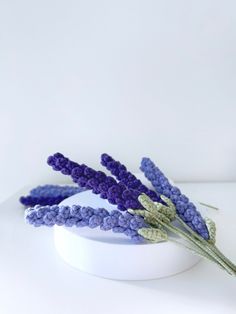 some purple flowers are sitting on a white table and it looks like they have been made out of crocheted yarn