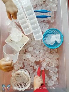 a child playing with ice cubes and plastic utensils in an ice tray