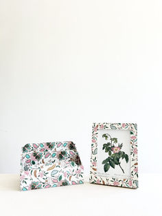 two small frames with flowers on them sitting next to each other in front of a white wall