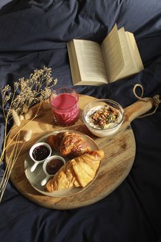 a breakfast tray with croissants, fruit and coffee on it next to an open book