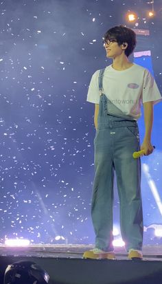 a young man standing on top of a stage wearing overalls and holding a yellow object