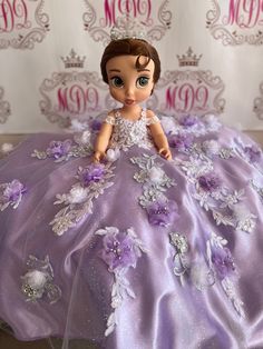 the doll is wearing a purple dress with flowers and pearls on it's skirt