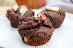 three chocolate cupcakes on a plate with an apple in the backgroun