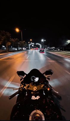 a motorcycle is driving down the street at night with its headlights on and lights on