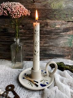 a white candle sitting on top of a table next to a vase with flowers in it