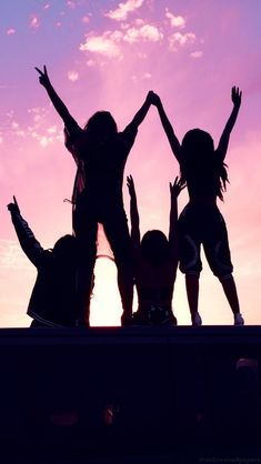 three girls are standing on the roof of a car with their arms in the air