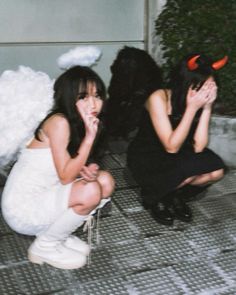 two women dressed up as devil and demon brides sit on the ground with their hands in their mouths