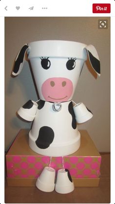 a toy cow sitting on top of a box with its head in the shape of a bucket