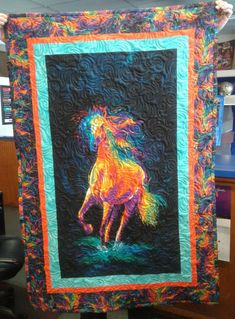 a person holding up a colorful quilt with a horse on it's front end