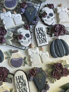 decorated cookies are arranged on a table with purple flowers and skeleton cookie cutters next to them