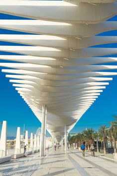 the walkway is lined with white columns and people walking under them on a sunny day