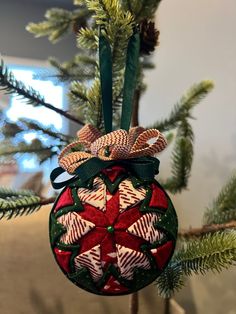 an ornament hanging from a christmas tree with pine cones and bows on it