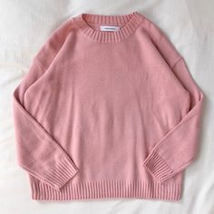 a pink sweater laying on top of a bed