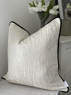 a white pillow sitting on top of a chair next to a vase filled with flowers