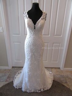 a white wedding dress on display in front of a door with a black mannequin