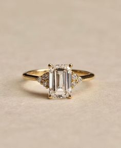 an emerald - cut diamond ring with three diamonds on the band, set in 18k yellow gold