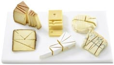 several different types of cheese on a cutting board with slices cut into squares and wedges