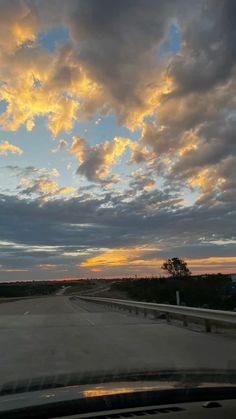 the sun is setting over an empty highway with clouds in the sky and trees on either side