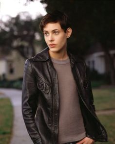 a young man in a black leather jacket is standing on the side walk with his hands in his pockets