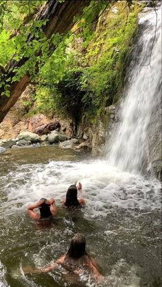 three people in the water near a waterfall