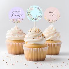 three cupcakes with white frosting and pink flowers on top are decorated with handwritten words