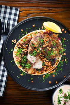 a black plate topped with meat covered in beans and garnish