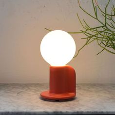 an orange table lamp sitting on top of a marble counter next to a potted plant