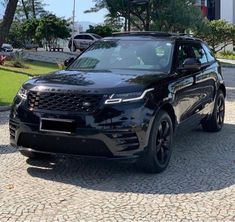 a black land rover is parked in front of some trees and bushes on a cobblestone street