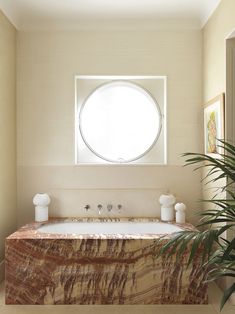 a bath tub sitting under a round window next to a potted palm tree in a bathroom