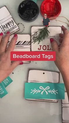 two hands are holding up some paper tags on a table with other items around it