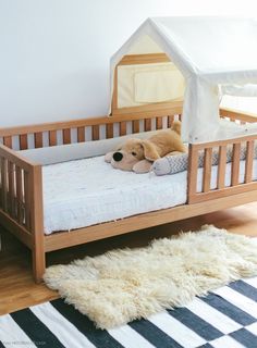 a teddy bear laying on top of a wooden crib next to a black and white rug