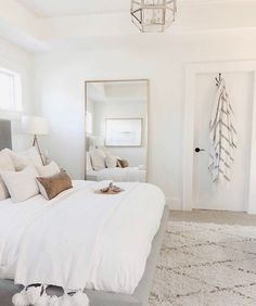 a bedroom with white bedding and pillows on top of the bedspread in front of a mirror